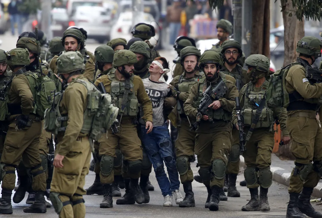 Israeli soldiers arrest Fawzi al-Juneidi, a Palestinian minor, in Hebron on December 7, 2017. Al-Juneidi is blindfolded and surrounded by a large crowd of nearly two dozen soldiers.