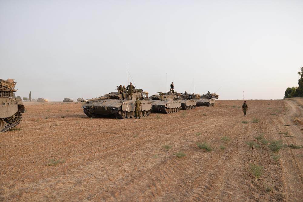 Israeli merkava tanks mobilized near the Gaza border, soldiers stand near and on the tanks. Image is from Israel's 2014 war on Gaza.