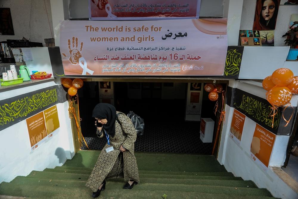 A Palestinian woman leaves an art exhibit dedicated to raising awareness regarding gender-based violence. With artwork on either side of the staircase leading to the exhibit entryway, a welcome banner reads "The world is safe for women and girls" in English and "under the slogan: women and girls feel hope at home, on the internet, on the street, at work, and in all segments of society" in Arabic. Rafah, Gaza Strip, 2019.