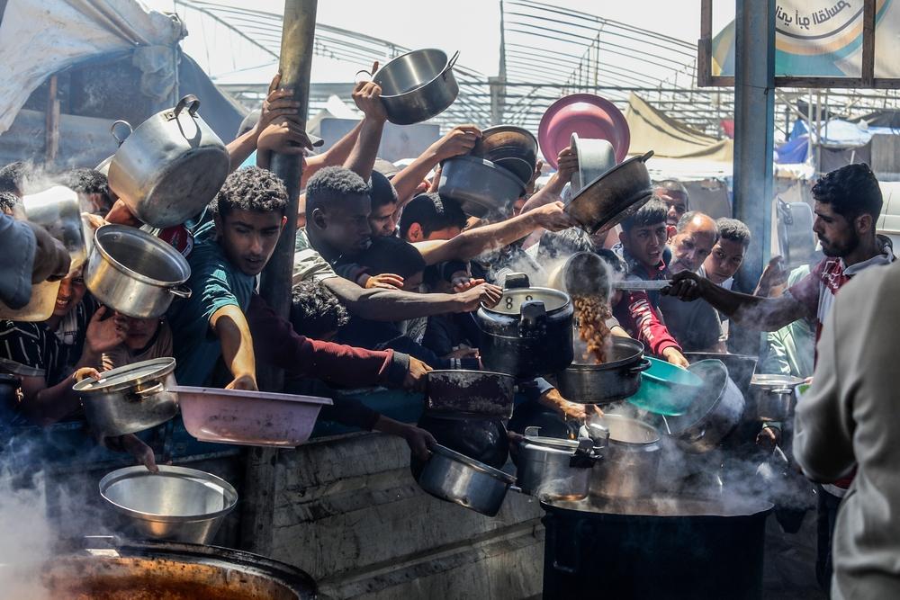 A large crowd of Palestinians carry pots and large bowls as aid workers distribute cooked meals in Mawasi, Khan Yunis as Israel's forced starvation of the Gaza Strip intensifies. April 2025.