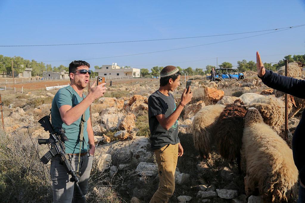 Armed Israeli settlers harass a Palestinian on his land in the West Bank.