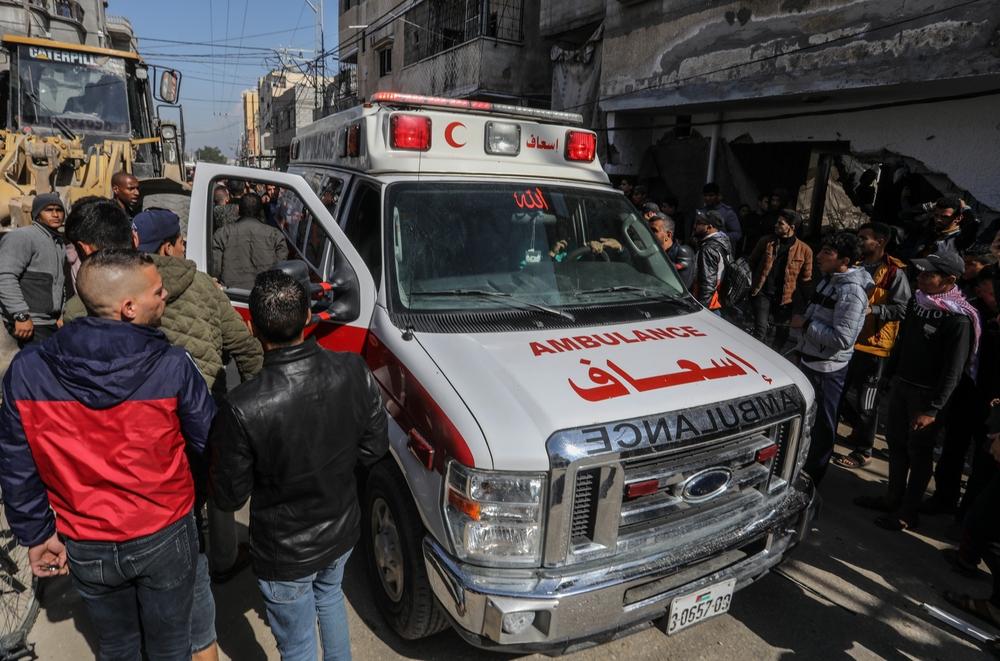 An ambulance arrives at the site of a house destroyed by an Israeli airstrike in Rafah as a large crowd looks on.