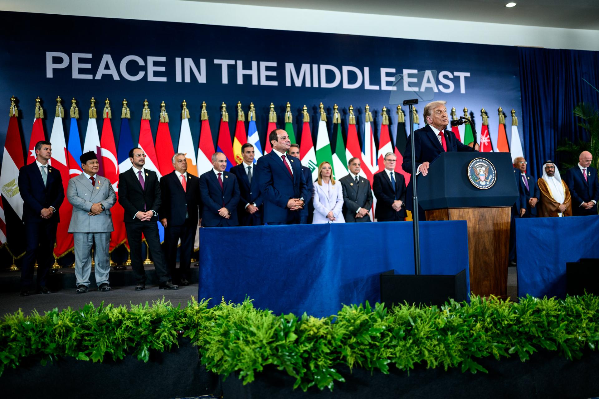 US President Donald Trump addresses the Sharm El Sheikh Summit in Egypt, joined on stage by Egyptian President Abdel Fattah El-Sisi and other world leaders. Behind them are flags belonging to states participating in the summit, and backdrop text reads "PEACE IN THE MIDDLE EAST."