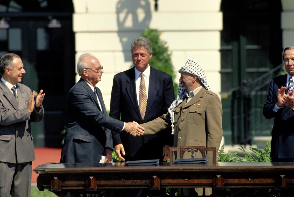 Palestine Liberation Organization (PLO) Chairman Yasser Arafat shakes hands with Israeli Prime Minister Yitzhak Rabin on the White House lawn as President Bill Clinton looks on for the signing of the First Oslo Accord (1993).