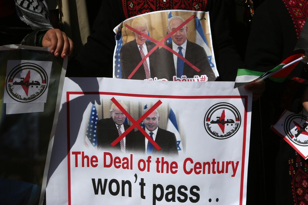 Signs held by protestors at a rally against the Trump Peace Plan, otherwise known as "Peace to Prosperity." One sign is a photo of Trump and Netanyahu marked by a large "x" another displays the same graphic of the leaders with English text that says "The Deal of the Century won't pass."