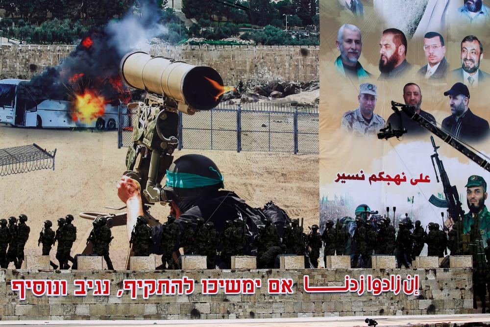 Banner image for the Hamas 31st anniversary celebration in Gaza City depicts a Qassam Brigades fighter firing an anti-tank missile on an Israeli bus on one side. On the other, commemorative photos of Hamas leaders that reads "we follow your path" in Arabic. At the bottom of the banner is the Arabic phrase "if they increase [attacks], we increase" and in Hebrew, the phrase "if they continue to attack, we will respond and increase [attacks]."