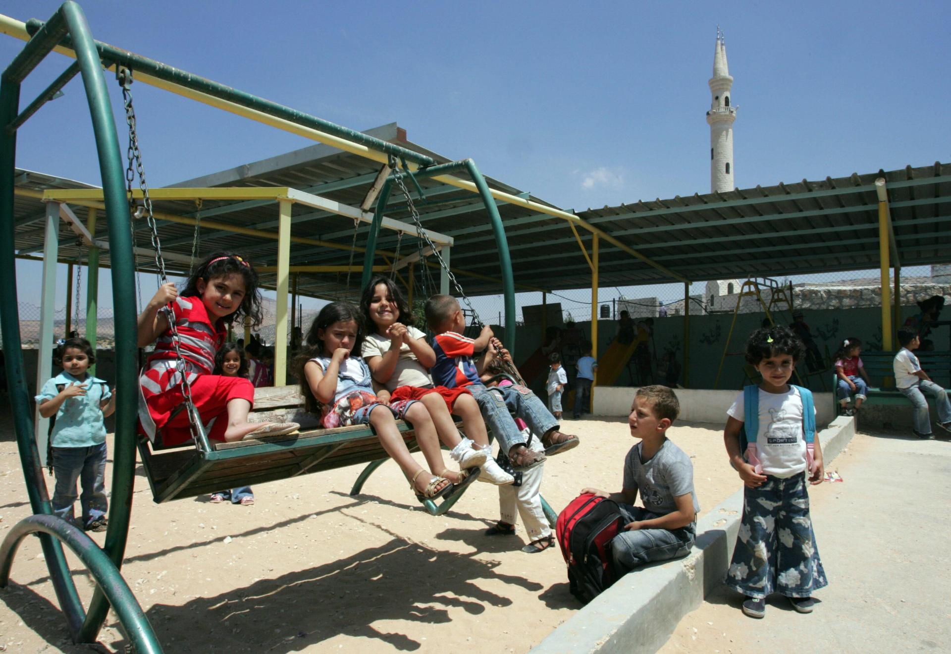Palestinian children stand and others sit on a swing on the grounds of the Aqaba kindergarten, which as of this 2008 photo, was under demolition orders from the Israel.