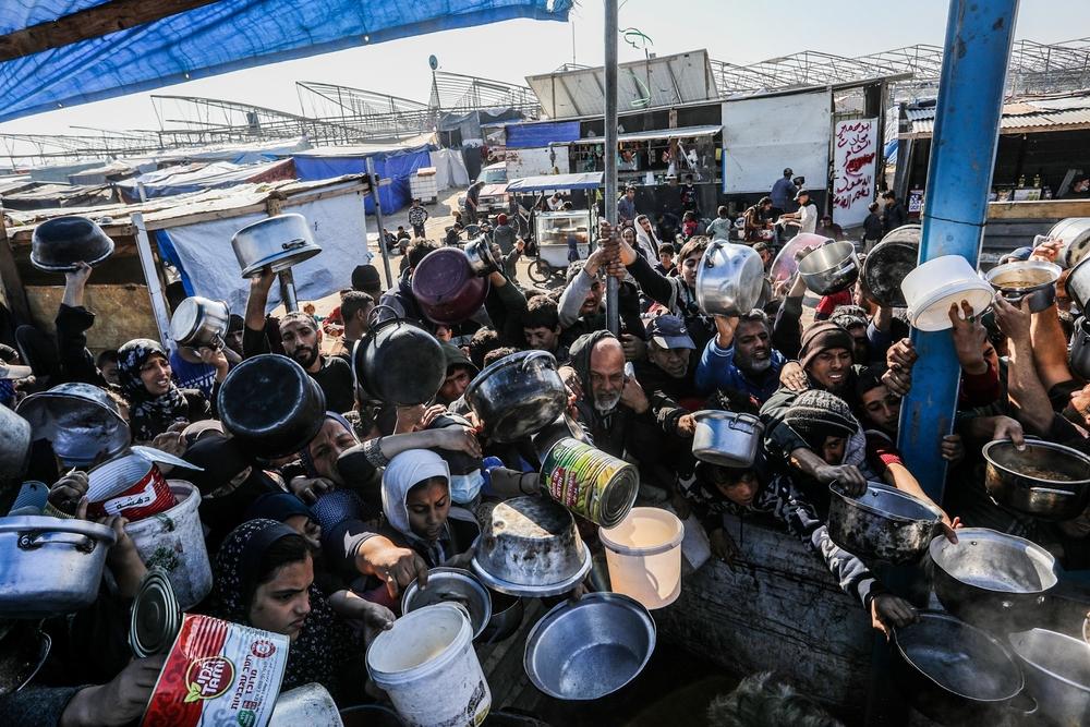 A large crowd of Palestinians carry pots, large cans, and large bowls and reach out for food from a meal distribution center as Israel's forced starvation of the Gaza Strip intensifies. January 2025.
