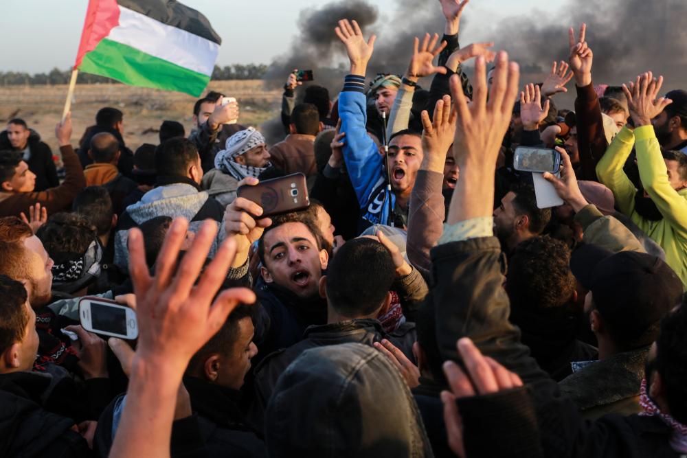 A large crowd of Palestinians participate in Gaza's Great March of Return at the Israel-Gaza border fence east of Rafah. Smoke rises in the background, as some protestors take photos and videos on their phones. January 25, 2019.