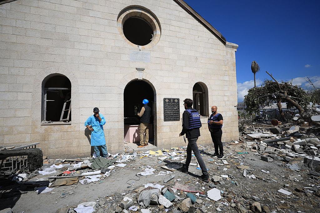 Officials from the UN Office for the Coordination of Human Rights (OCHA), wearing protective vests marked OCHA, inspect damage to the Ahli Baptist Hospital co from the UN Office for the Coordination of Human Rights (OCHA), wearing protective vests marked OCHA, inspect damage to the Ahli Baptist Hospital compound in Gaza City, pictured here as they walk into the church. The surrouding area to the church's entrance is surrounded by rubble and two destroyed trees, its church's stained glass windows are broken.