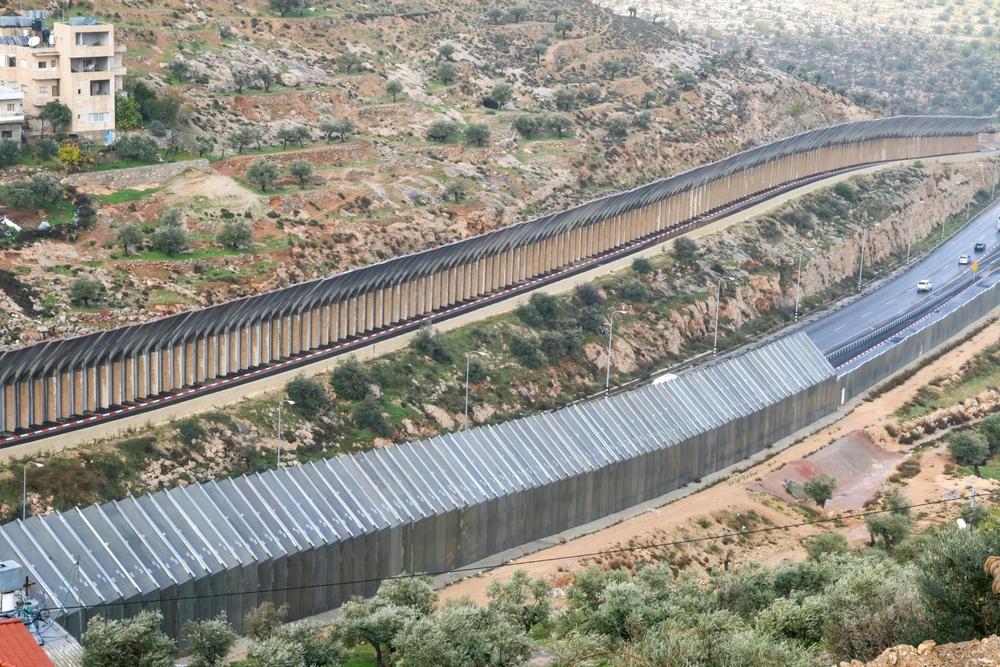 A view of Israel's apartheid wall, with metal fencing and concrete walls, running alongside Israeli highway Route 60.