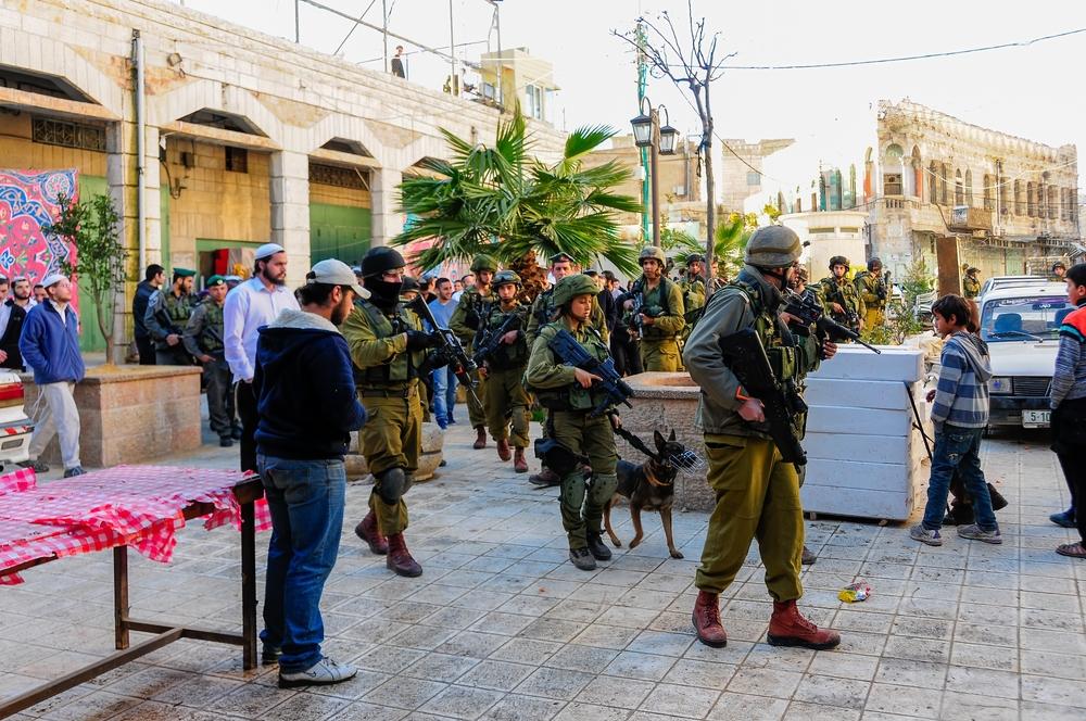 A large crowd of Israeli soldiers carrying weapons, including one attack dog, guard a group of Israeli settlers walking through the Palestinian city of Hebron in the West Bank.