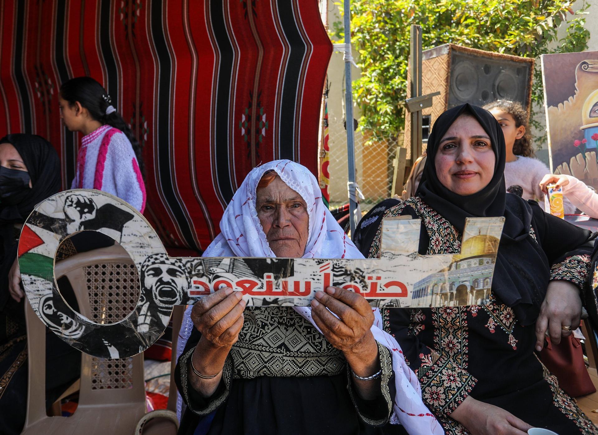 A Palestinian elderly woman holds a sign in the shape of a key, a symbol of the Palestinian right of return to their original homes, that says in Arabic: "inevitably, we will return."