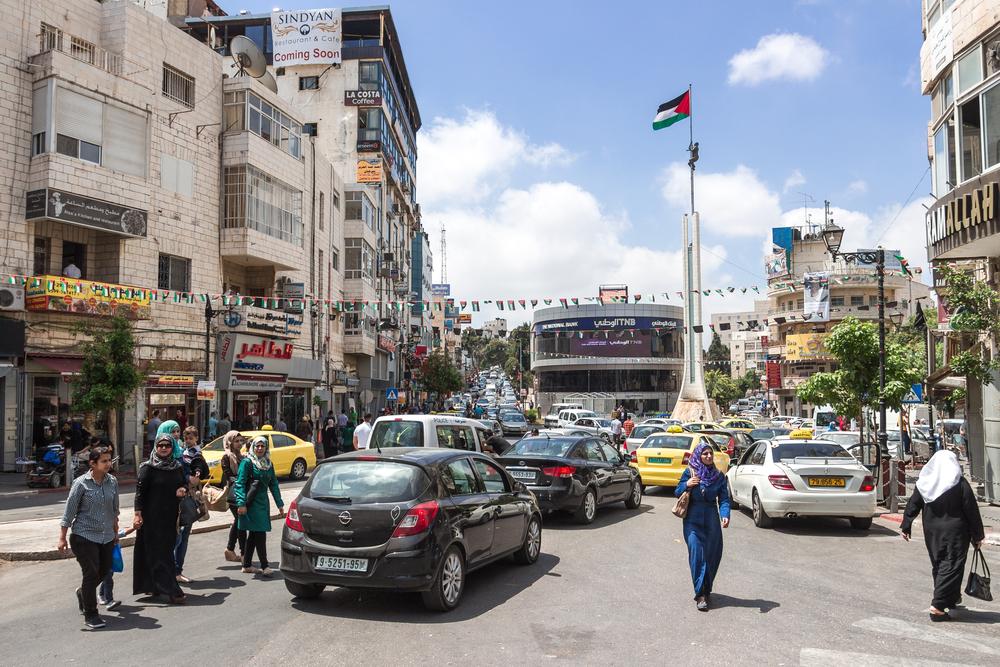 Palestinians walk through a busy, traffic-filled road in downtown Ramallah.