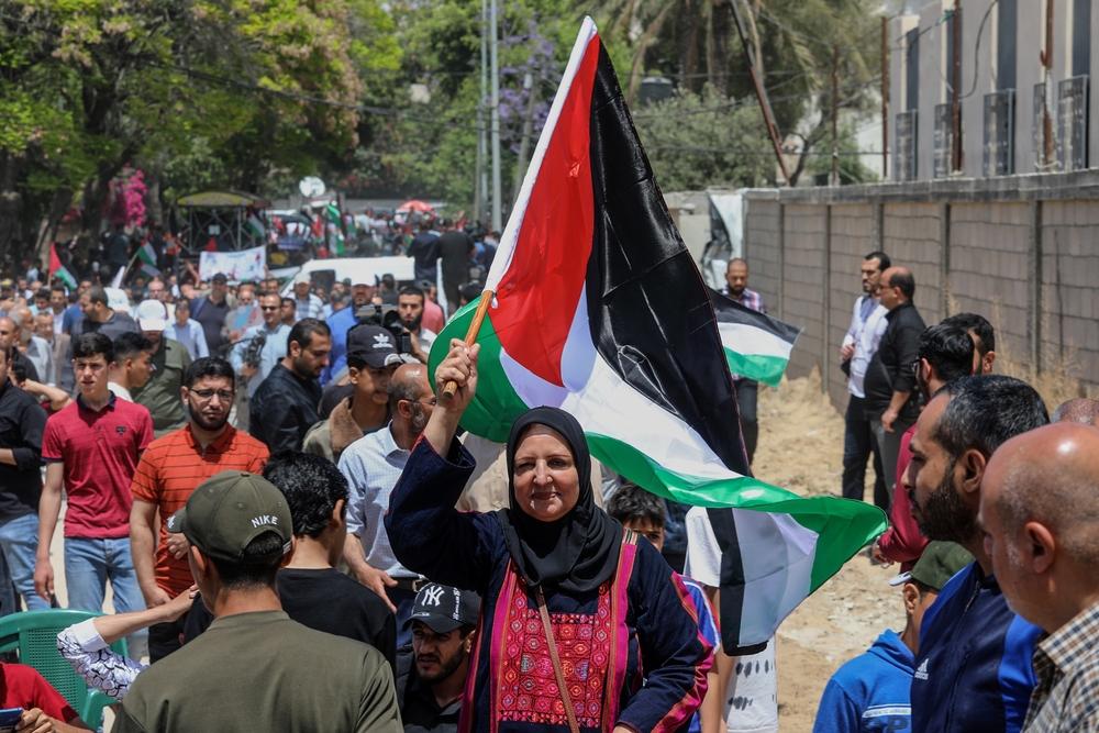 At a rally commemorating the 74th anniversary of the Nakba, a Palestinian woman wearing a traditional thobe waves a Palestinian flag.
