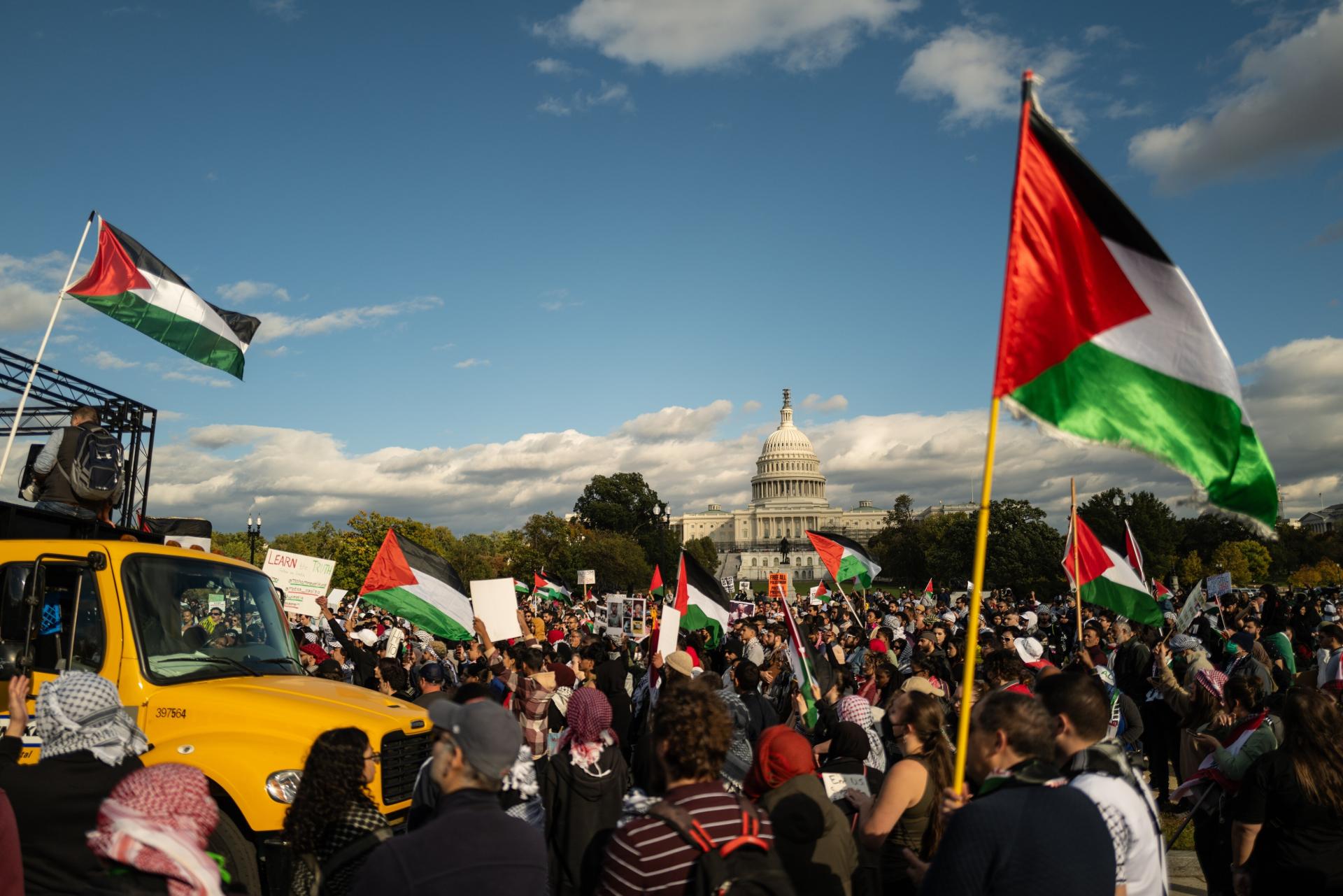 Large protest demanding a ceasefire in Gaza with the US Capitol Building in view. Many protestors carry Palestinian flags and wear kuffiyehs.