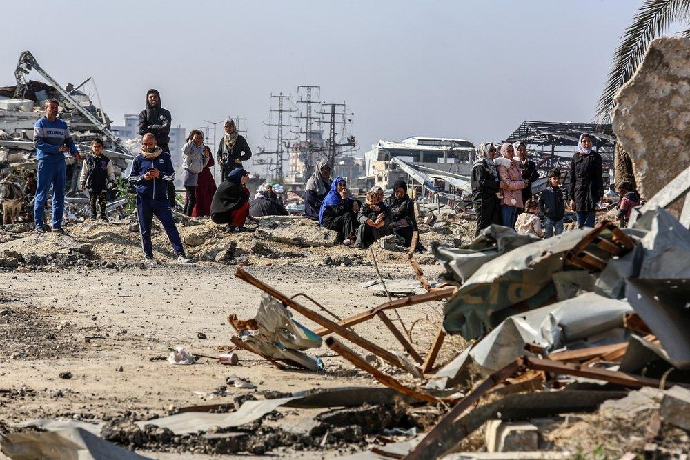 Displaced Palestinians returning to their homes in Gaza City stand on the road amid the ruins.