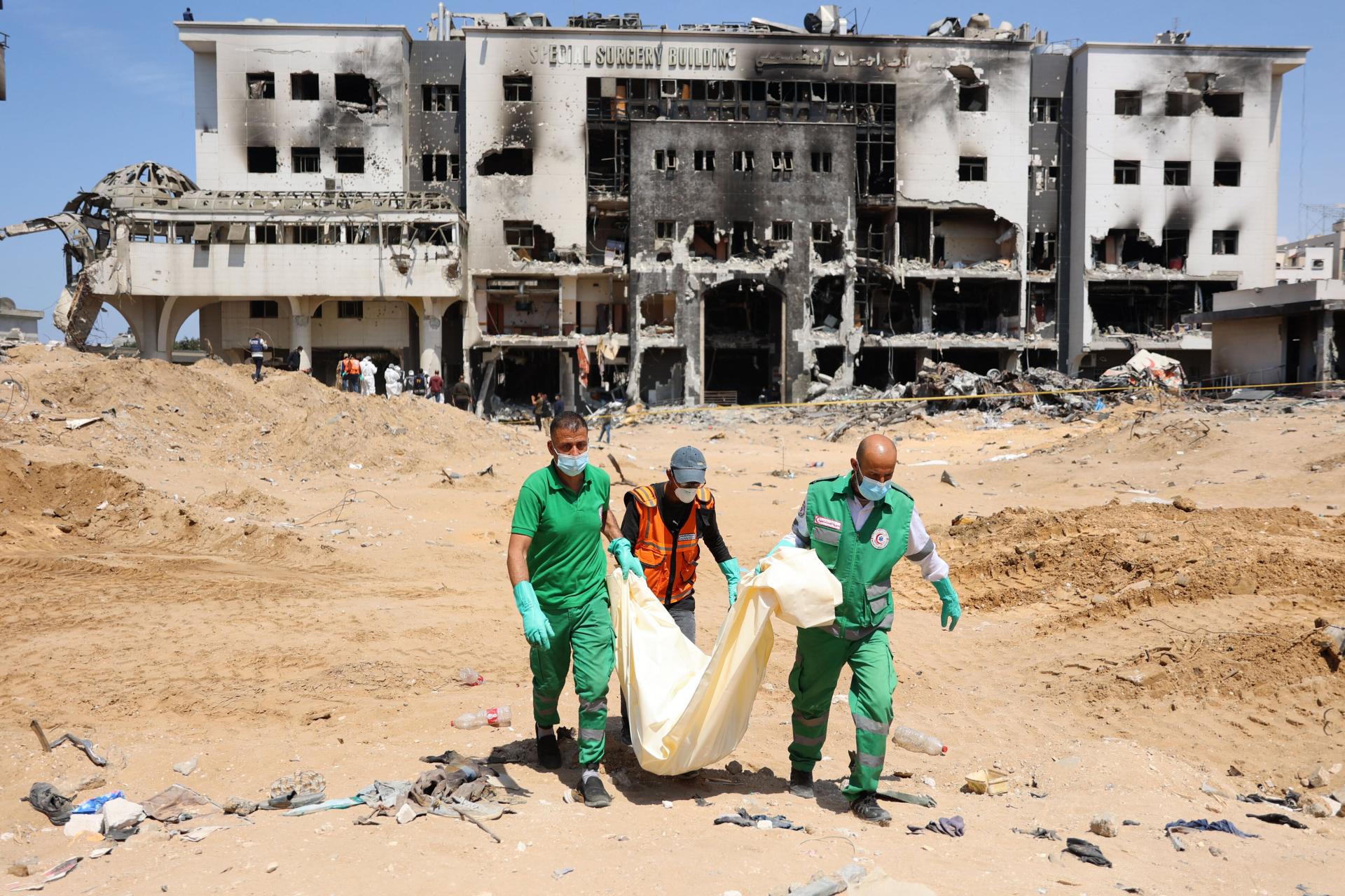 Forensic and civil defense teams carry a body covered in a shroud as teams search for bodies at a mass burial site at Gaza's al-Shifa hospital after Israel's two-week raid which reduced much of the hospital compound to rubble.