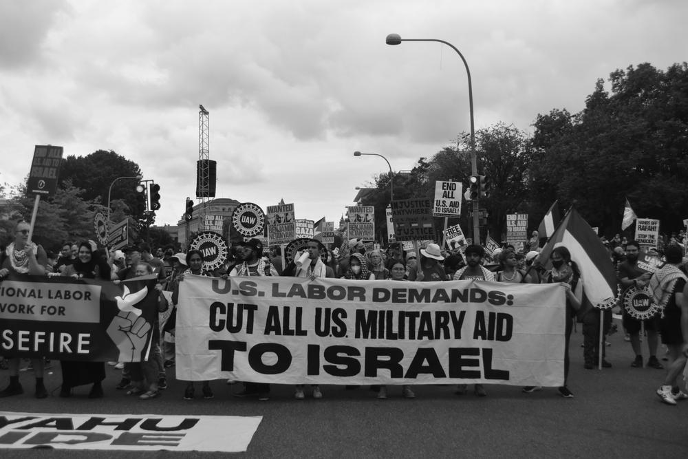 Labor organizers hold a banner that says "U.S. LABOR DEMANDS: CUT ALL US MILITARY AID TO ISRAEL" and others carry signs that say "UAW" (United Auto Workers) and "END ALL U.S. AID TO ISRAEL!"