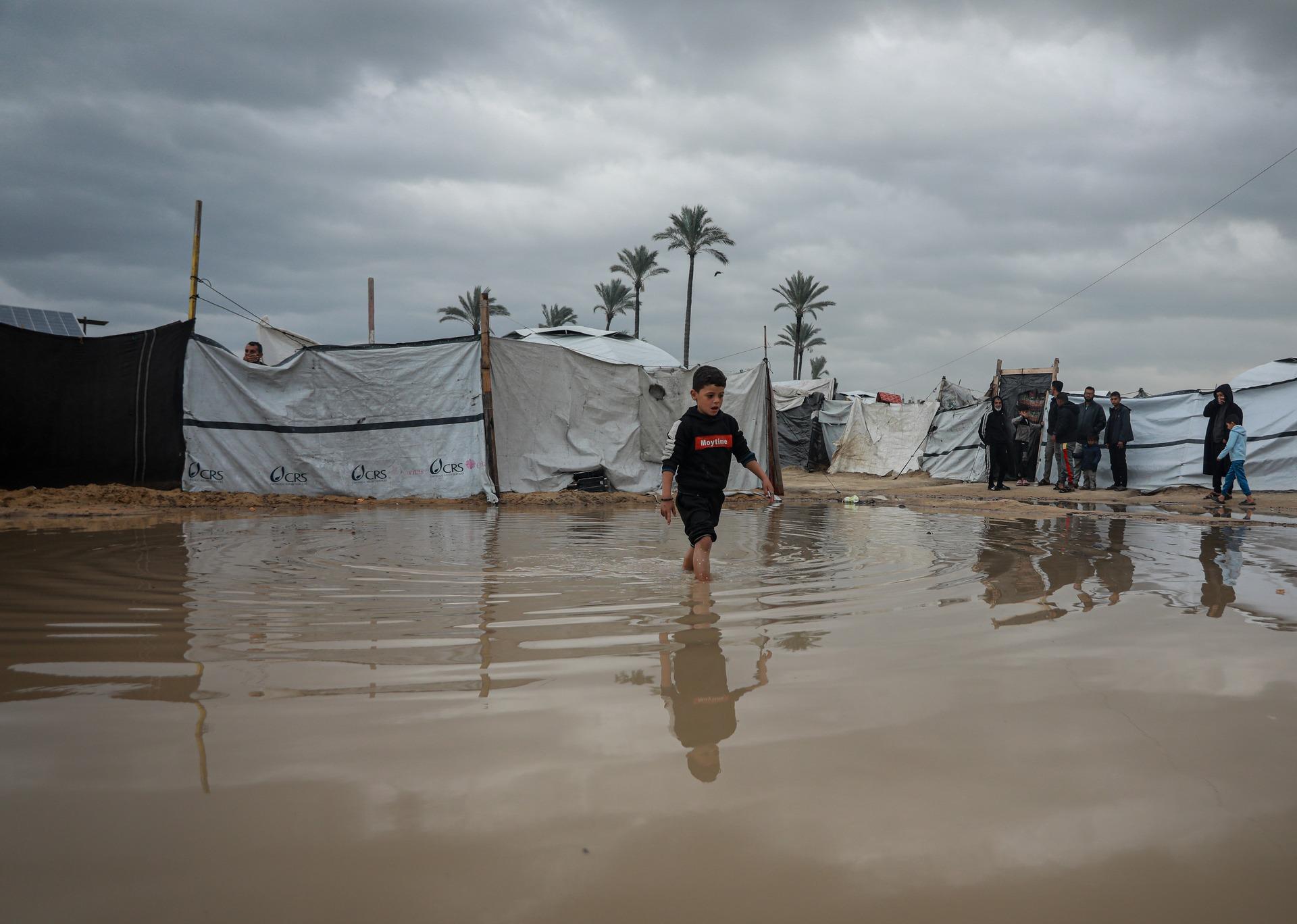A Palestinian boy walks through a high puddle left from severe flooding in Gaza near displacement tents where Palestinians struggled to endure harsh winter conditions.