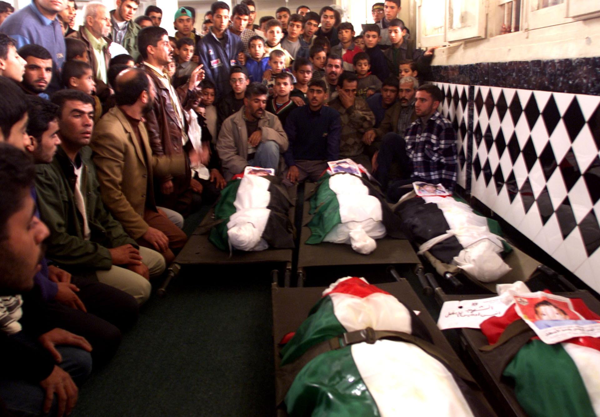 Mourners perform funeral prayers for five Palestinian boys who were killed by an Israeli tank shell ordnance in the Khan Yunis Refugee Camp. Their burial shrouds are draped in Palestinian flags, with photos of each child. November 2001.