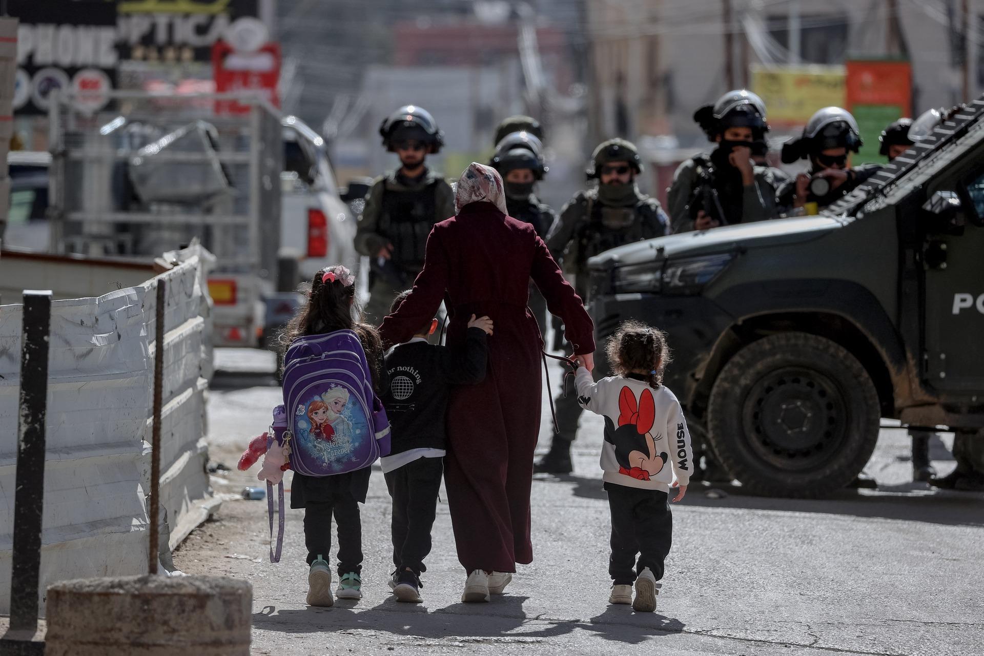 A mother with three small children come face-to-face with a large group of armed Israeli soldiers as they walk in their town, as Israel raids the Qalandia refugee camp and the town of Kafr `Aqab.