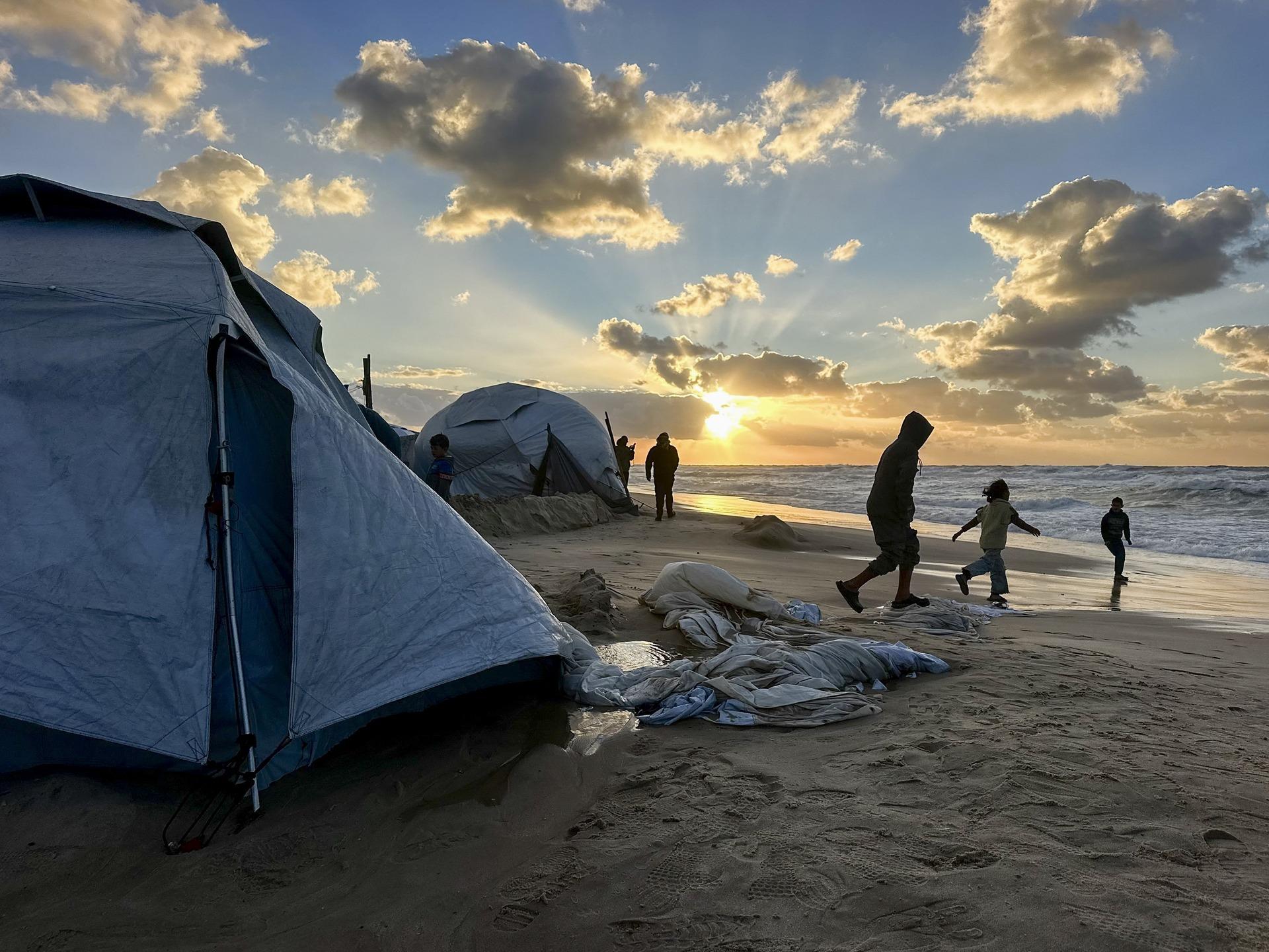 Displaced Palestinians walk near tents on the beach in Khan Yunis on a cold winter day. December 28, 2025.