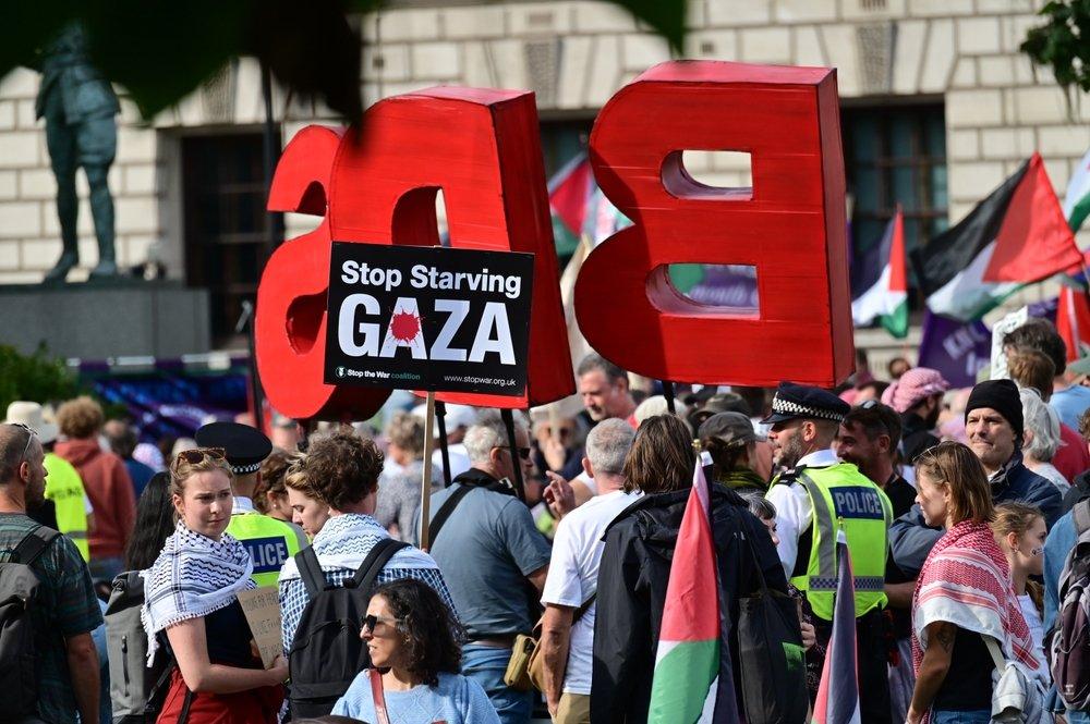 At a rally in London, a protestor holds a sign that says "Stop Starving Gaza" as others carry Palestinian flags and extra large letters that read "BDS."