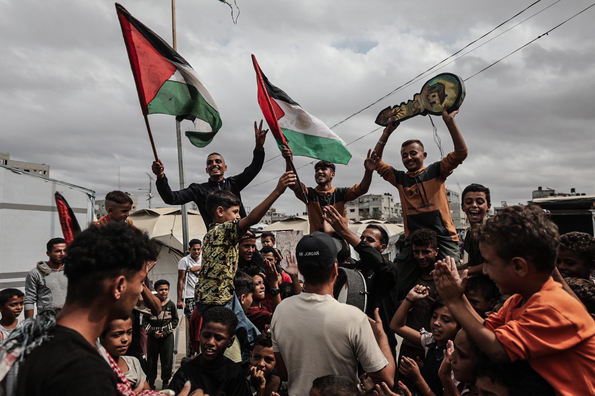 Palestinians in the Nuseirat refugee camp celebrate the announcement of a ceasefire agreement in Gaza. They carry Palestinian flags and a key with illustrations symbolizing the Palestinian right of return. October 9, 2025.