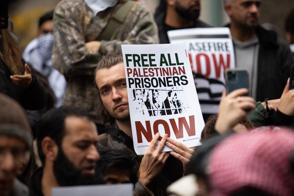 A protestor carries a sign that reads "FREE ALL PALESTINIAN PRISONERS NOW."