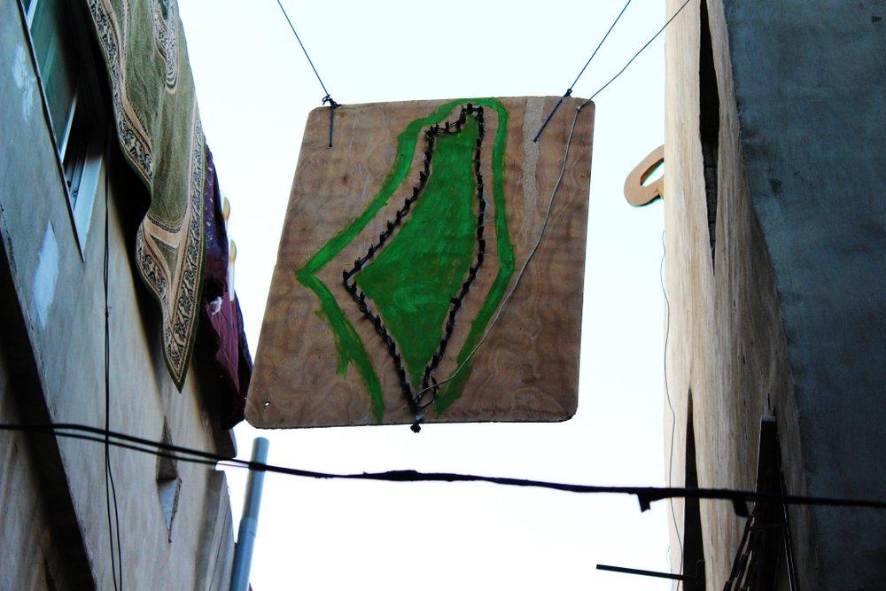 Artwork depicting the map of historic Palestine hangs between two buildings on a narrow street in a Palestinian refugee camp in Jordan.