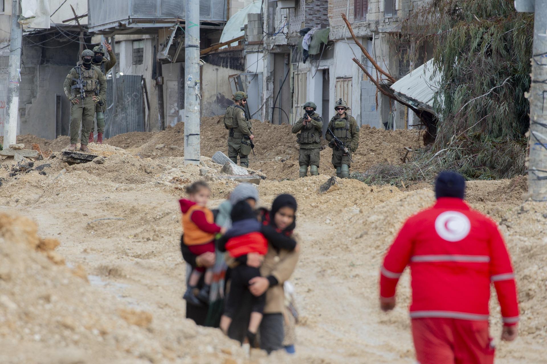 Palestinian women carry small children as they walk over rubble in the Nur Shams refugee camp as Israeli soldiers look on, in the midst of their ethnic cleansing of the camp. February 10, 2025.
