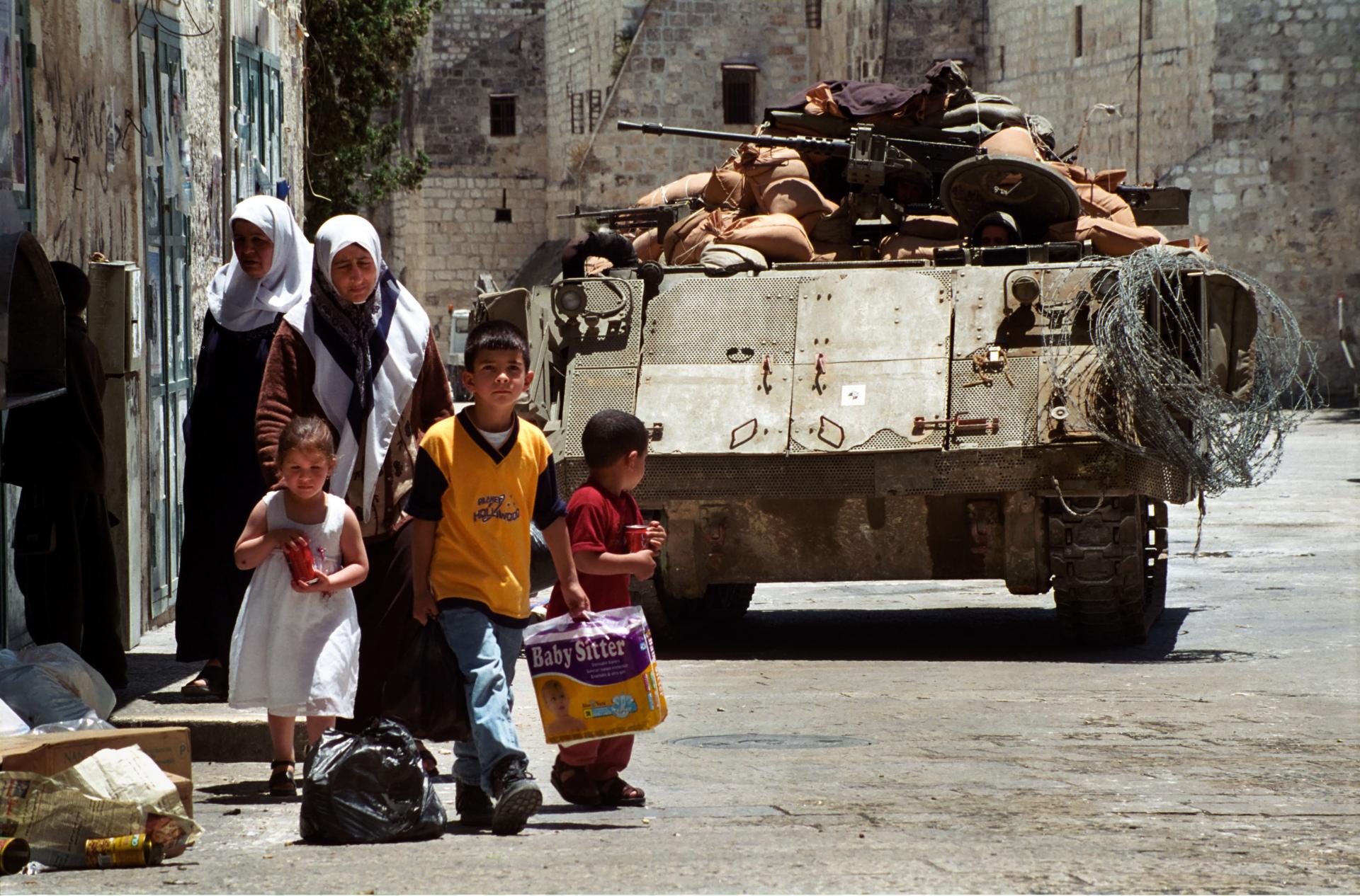 Palestinian women and three small children walk down a street in Bethlehem with an Israeli tank closely behind them in this photo from the Second Intifada, dated May 28, 2002.