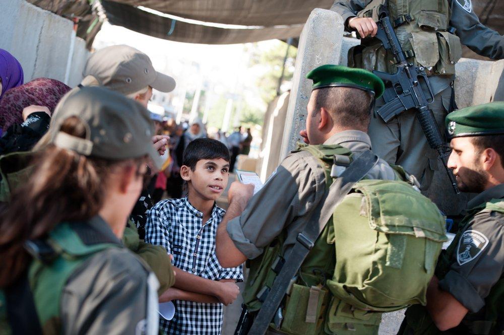 A Palestinian boy stands as an Israeli soldier checks his ID as he waits to cross a checkpoint from Bethlehem to travel to Jerusalem.