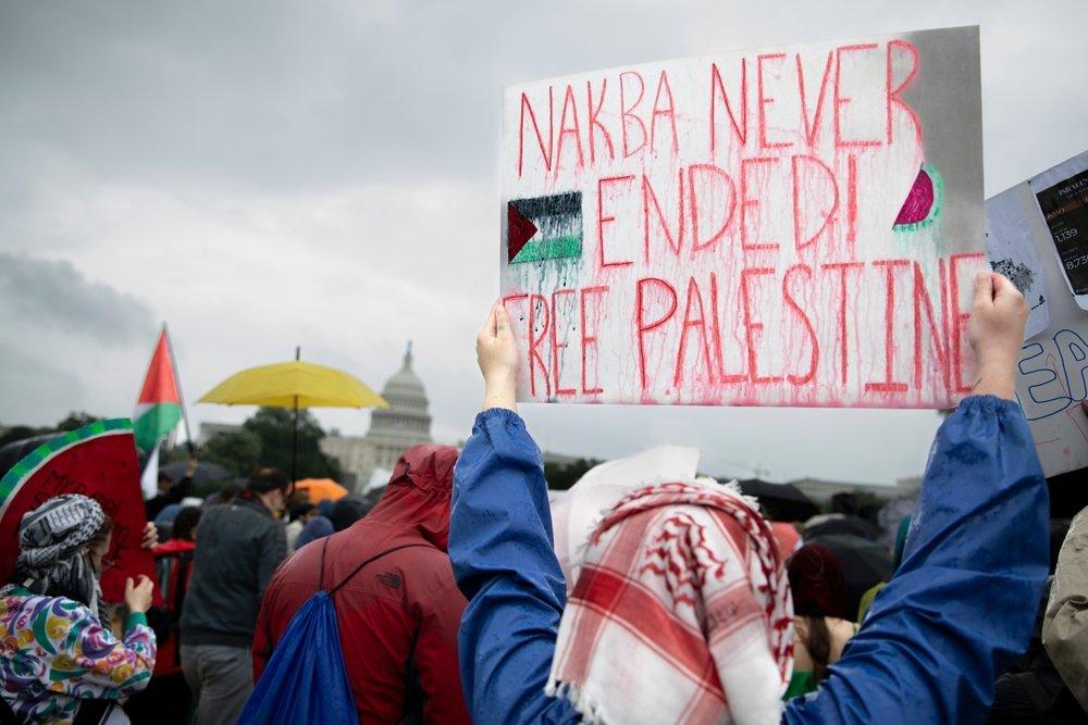 A protestor holds up a sign that says "NAKBA NEVER ENDED! FREE PALESTINE."