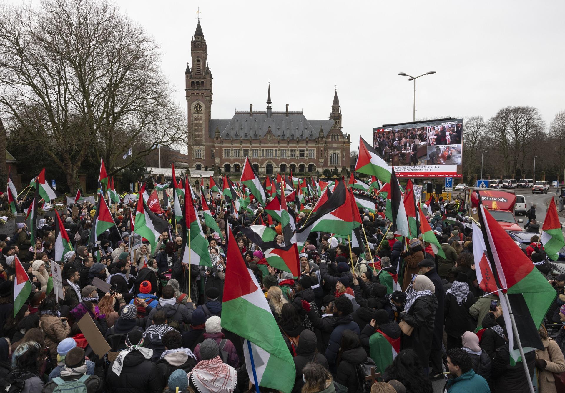 Protestors rally outside of the International Court of Justice (ICJ) in support of South Africa's case against Israel for the crime of genocide in Gaza, as they wave Palestinian flags and watch the proceedings on a large screen.