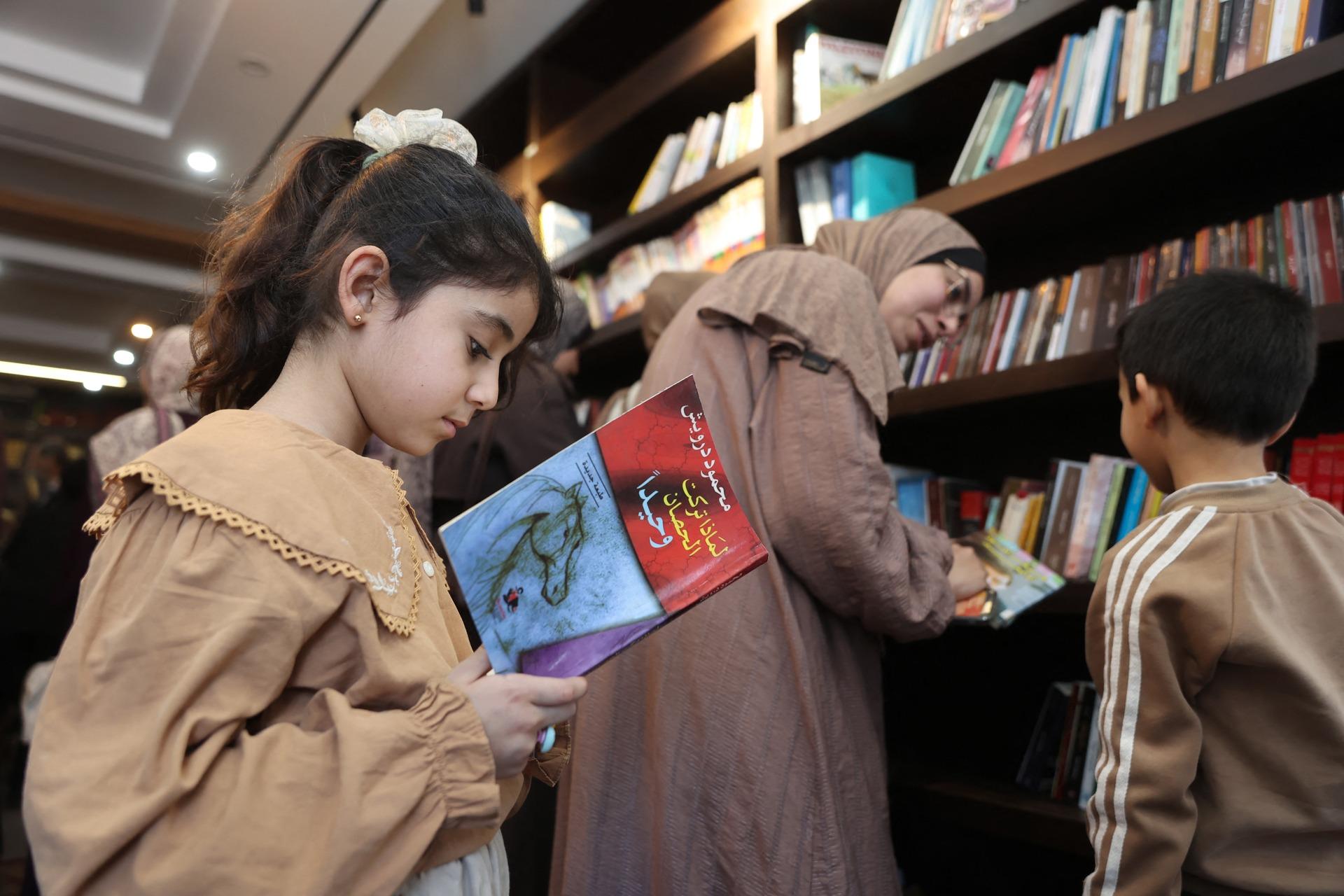 A Palestinian girl reads a copy of Mahmoud Darwish's "Why Did You Leave the Horse Alone?" at the Al-Ankaa (Phoenix) Library in Gaza City. April 21, 2026.