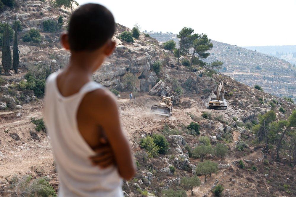 A Palestinian boy looks on the Israeli mliitary uses Caterpillar equipment to clear out Palestinian land to make way for the construction of Israel's apartheid wall near the town of al-Walaja in the occupied West Bank. September 5, 2001.