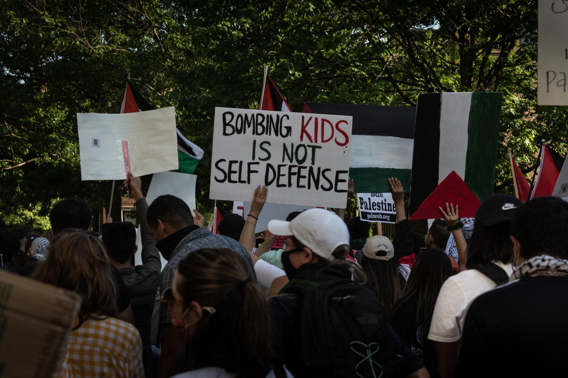 At a rally outside of the Israeli Embassy in Washington DC during the 2021 war on Gaza, a protestor carries a sign that says "BOMBING KIDS IS NOT SELF DEFENSE."