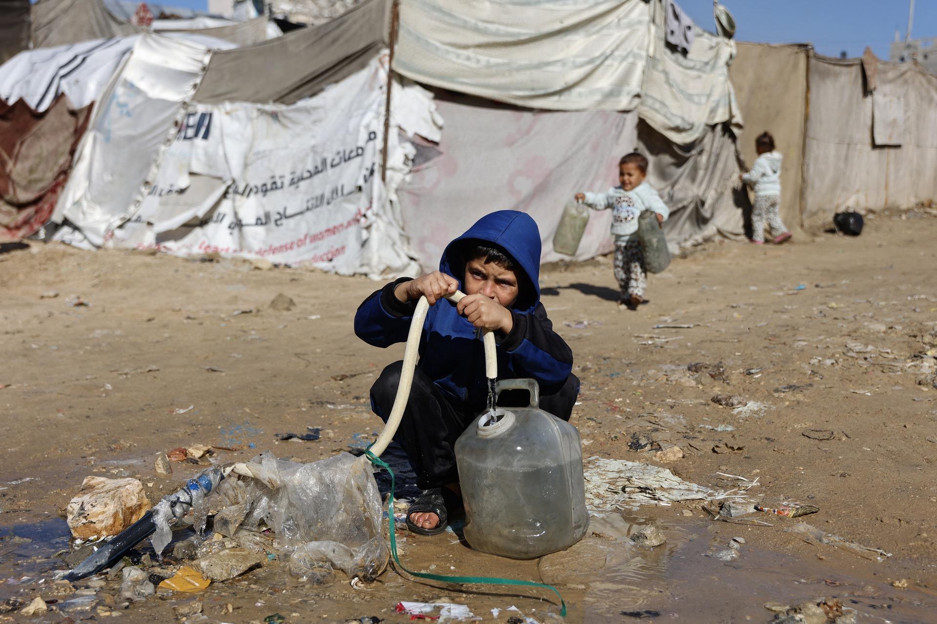 A child fills water into a container in a displacement camp with makeshift tents during harsh winter conditions in the Gaza Strip. January 11, 2026.