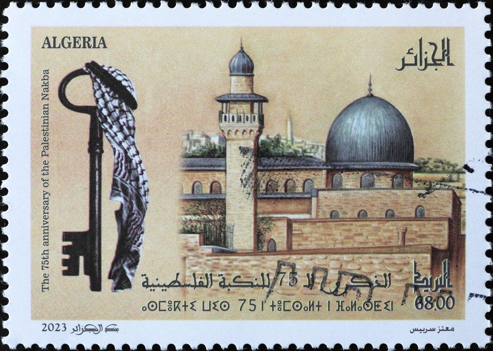 An Algerian postage stamp issued in 2023, commemorating the 75th anniversary of the Palestinian Nakba, by artist Motaz Saryis, contains an illustration of the Qibli Mosque in the Al-Aqsa Mosque compound in Jerusalem beside a key symbolizing the Palestinian right of return, draped in a kuffiyeh. Stamp contains writing in English, Arabic, and the Tamazight (Algerian Amazigh) language.