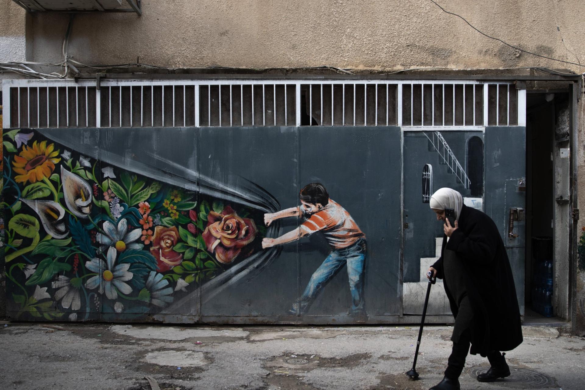 A woman walks in front of a graffiti in the Silwan neighborhood, located south of Al-Aqsa Mosque, as Palestinians are struggling to continue their lives under harsh conditions due to Israeli home demolitions and eviction orders in East Jerusalem on December 31, 2025. 