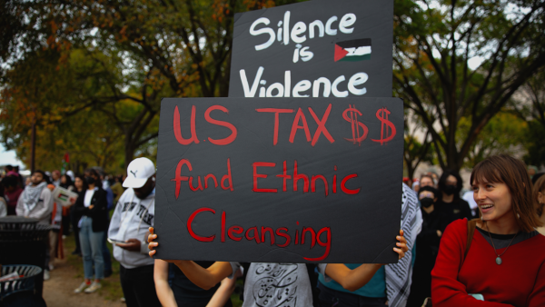 Protestor carries sign that says "Silence is Violence - US Tax $$ Fund Ethnic Cleansing" 