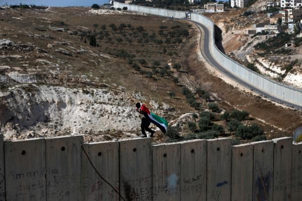 A man draped in the Palestinian flag walks on top of Israel's apartheid wall