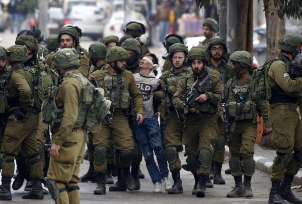 Israeli soldiers arrest Fawzi al-Juneidi, a Palestinian minor, in Hebron on December 7, 2017. Al-Juneidi is blindfolded and surrounded by a large crowd of nearly two dozen soldiers.