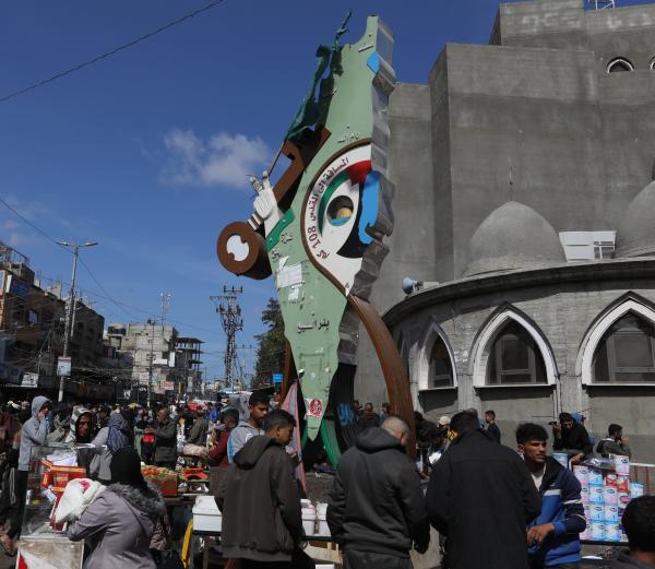 Displaced Palestinians shop at a market in Rafah near a statue marking "Return (`Awda) Square," displaying a map of historic Palestine, a key symbolizing the right of return, that marks the 108-kilometer distance from the landmark in Rafah to Jerusalem.