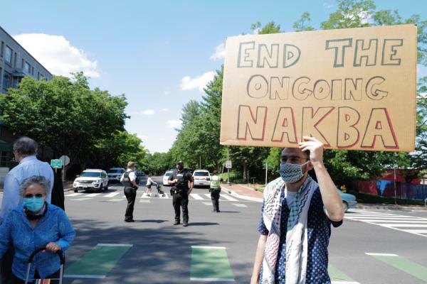 At a protest near the Israeli Embassy in Washington DC during its 2021 war on Gaza and attacks on Jerusalem, a protestor holds up a sign that says "End the Ongoing Nakba."