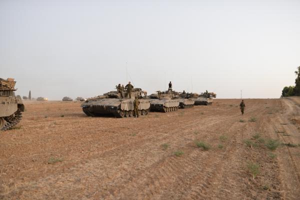 Israeli merkava tanks mobilized near the Gaza border, soldiers stand near and on the tanks. Image is from Israel's 2014 war on Gaza.