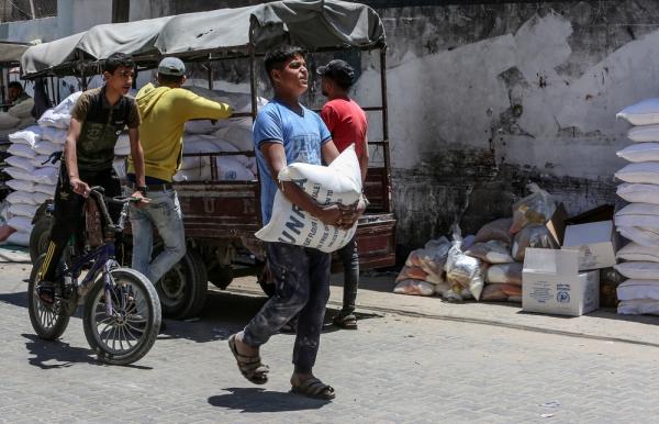 Palestinians collect food aid from an UNRWA distribution center in Rafah, a youth carries a flour sack.