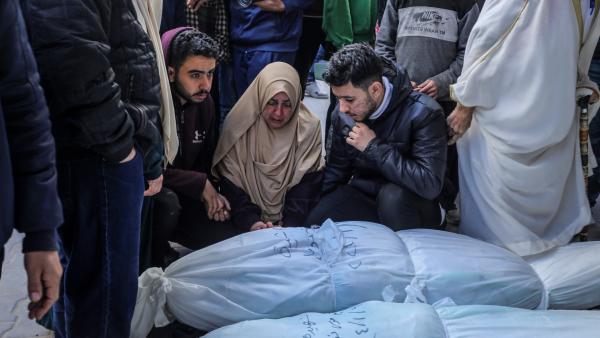 Palestinian families sit and stand over the bodies of their family members, wrapped in burial shrouds and with their names hand-written in black ink, outside of Al-Najjar Hospital in Rafah after an Israeli airstrike. January 10, 2024.
